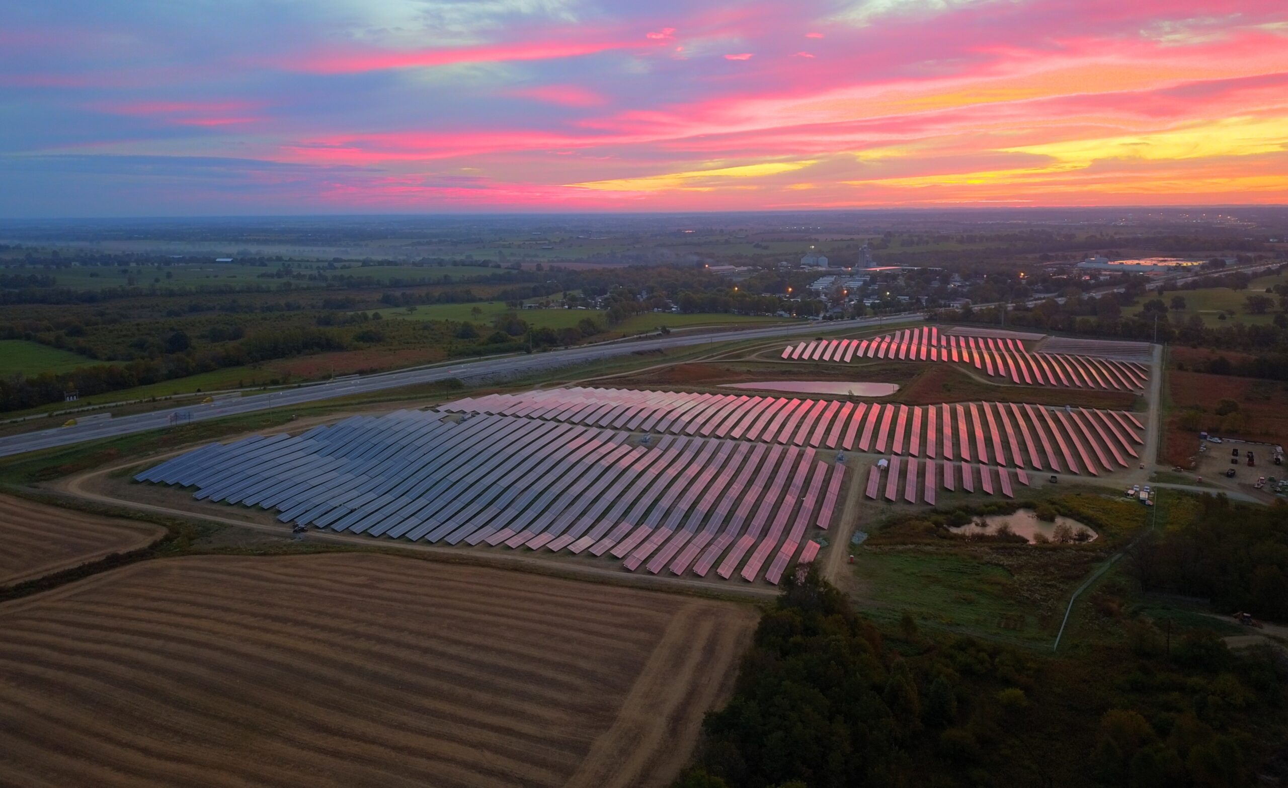 An expansive solar farm seen from above, featuring neatly arranged solar panels capturing the last rays of sunlight during sunset.